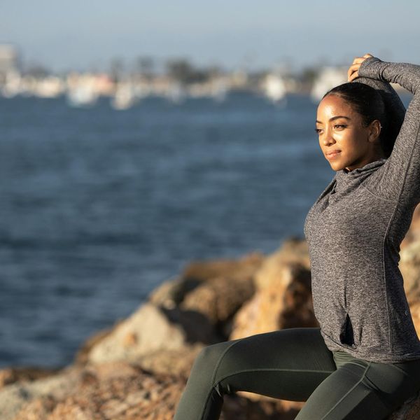 Person stretching peacefully at sunrise, silhouette against a calm background.