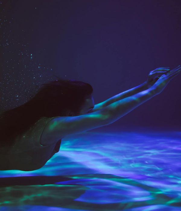 Woman performing a fluid, energetic movement in a dark room with blue light.